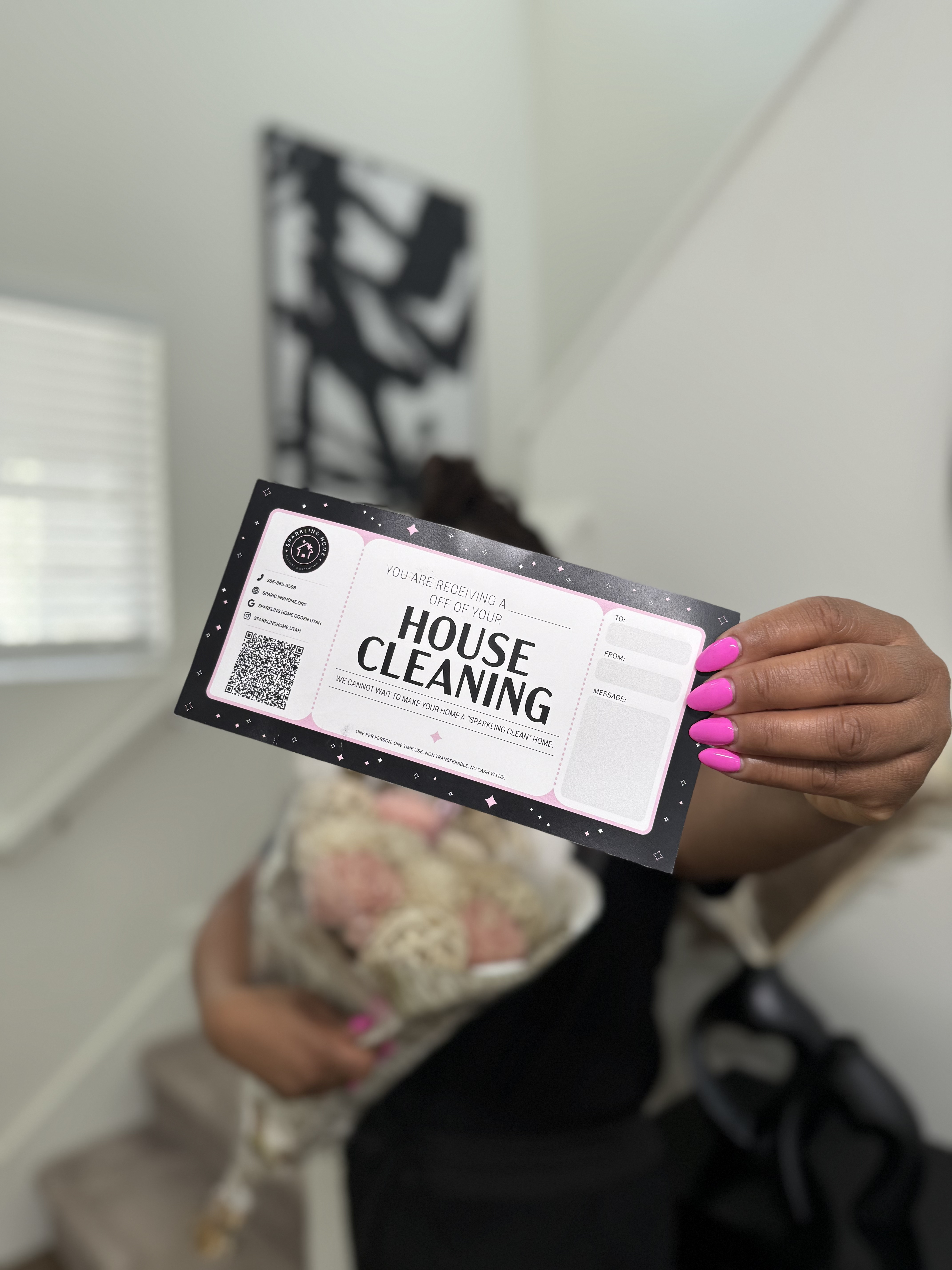 Woman holding a house cleaning gift card and a bouquet of flowers, standing on a staircase